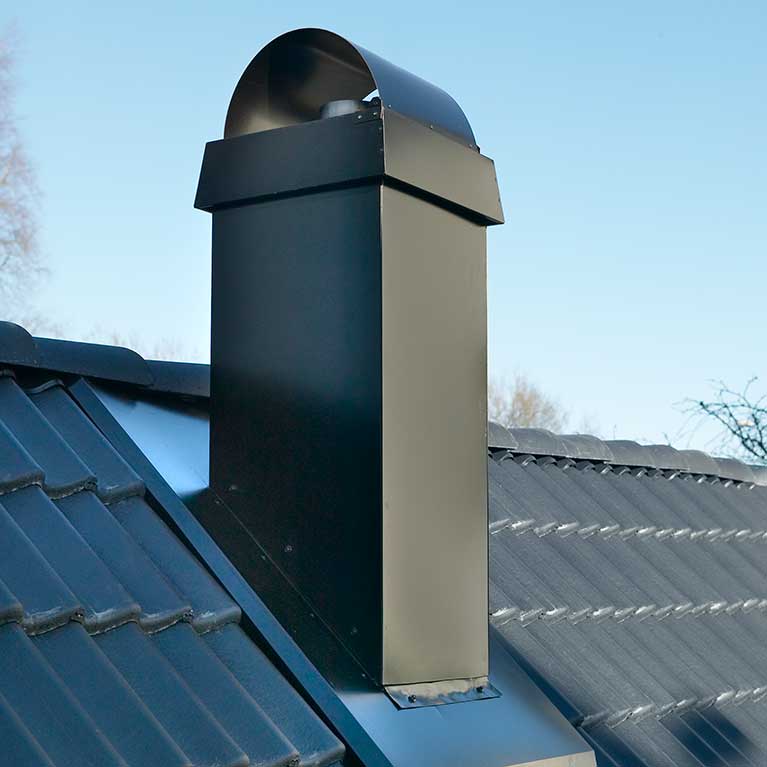 En svart metallskorsten med ett böjt lock är monterad på ett sluttande tak täckt med mörka plattor, vilket illustrerar hur att installera kamin utan murstock kan förbättra ditt hems design mot en klarblå himmel.