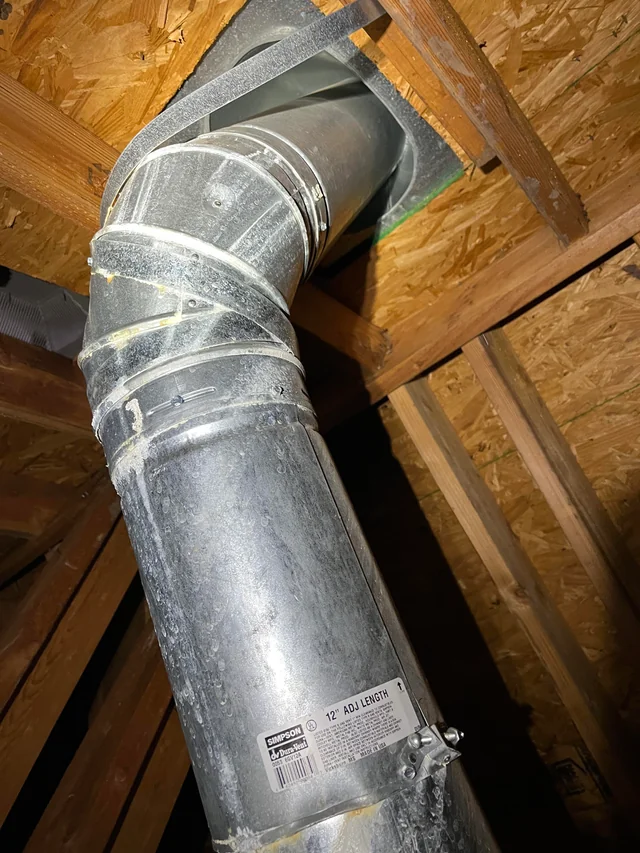 Vanliga fel vid installation (och hur du undviker dem) 4 En luftkanal av metall på en vind är fäst med buntband i träbjälkar, med isolering och byggmaterial synliga runtomkring. På en etikett på kanalen står det 12 ADJ. LÄNGD.