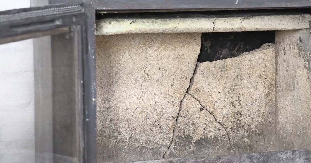 Närbild av en sprucken vägg eller platta i en glasmonter, med stora sprickor och åldrad, väderbiten ytstruktur.